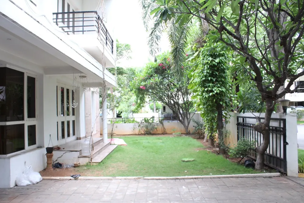 Side lawn and paved patio of the Aparna Cyber County villa, beneath the trees